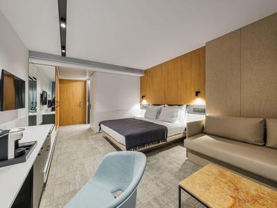 Chambre d'hôtel moderne avec lit double, canapé et bureau aux tons doux.