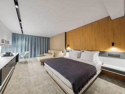 Chambre d'hôtel moderne avec lit double, mur d'accent en bois, canapé et rideaux gris.