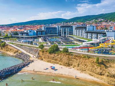 Complejo hotelero moderno con piscina grande y toboganes acuáticos junto a una costa rocosa con playa