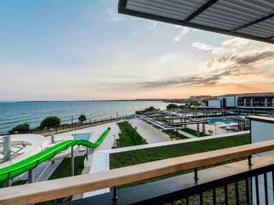 Vista desde un balcón de un moderno complejo hotelero con tobogán acuático y mar al fondo al atardecer.