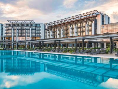 Complejo hotelero moderno con gran piscina exterior y tumbonas al atardecer.