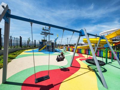 Aire de jeux colorée avec balançoires, structures d'escalade et toboggans aquatiques sous un ciel bleu