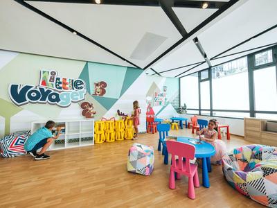 Salle de jeux colorée pour enfants avec tables, chaises et poufs dans un espace lumineux.