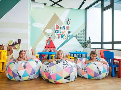Trois enfants assis sur des poufs colorés dans une pièce lumineuse et ludique avec des meubles pour enfants.