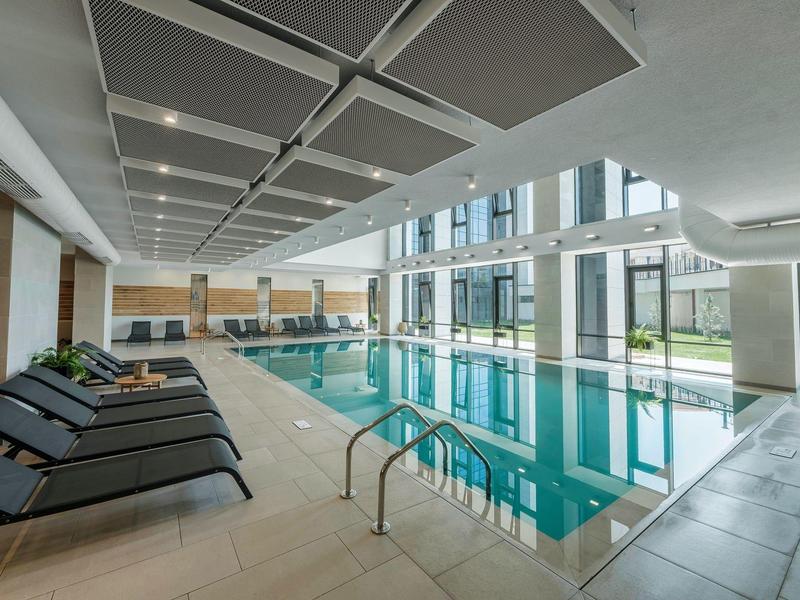 Piscine intérieure moderne d'hôtel avec chaises longues et grandes fenêtres donnant sur le jardin.