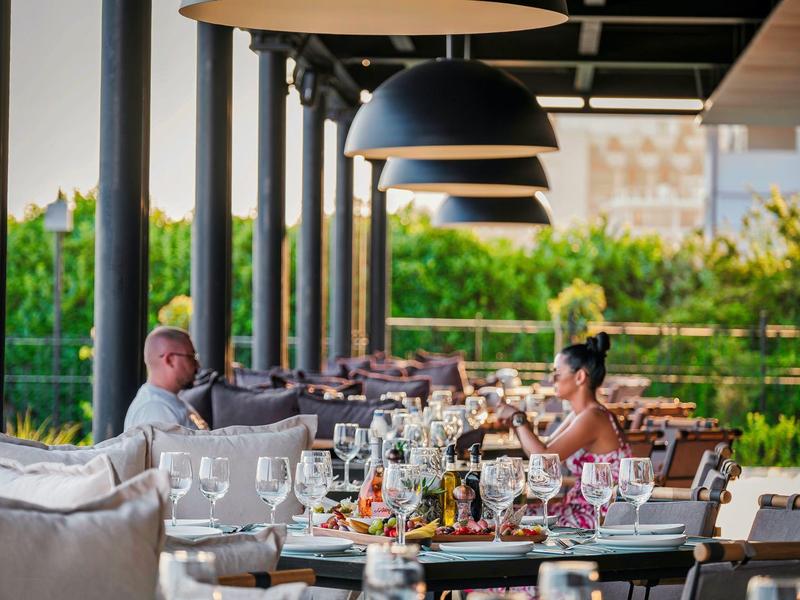 Espace terrasse avec tables dressées et deux personnes dans une ambiance de vacances détendue.