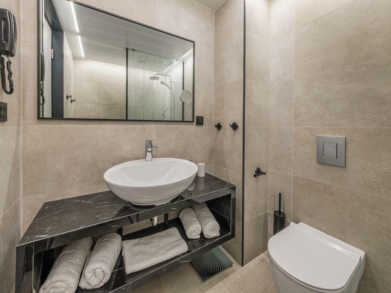 Salle de bain moderne avec lavabo, grand miroir, serviettes et toilettes.