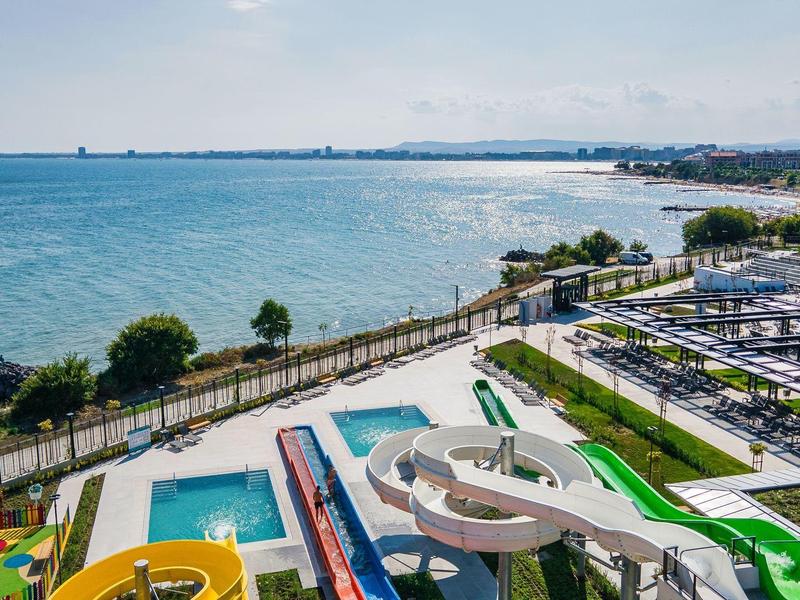 Vue d'un parc aquatique avec toboggans et piscines au bord de la mer par temps ensoleillé.