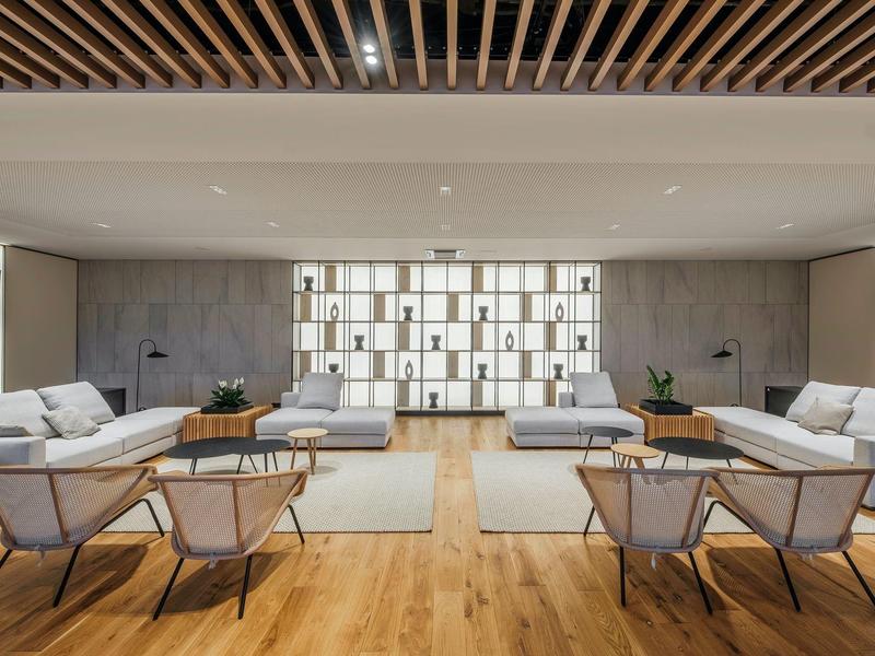 Salon d'hôtel moderne avec fauteuils gris et sol en bois sous un plafond blanc.
