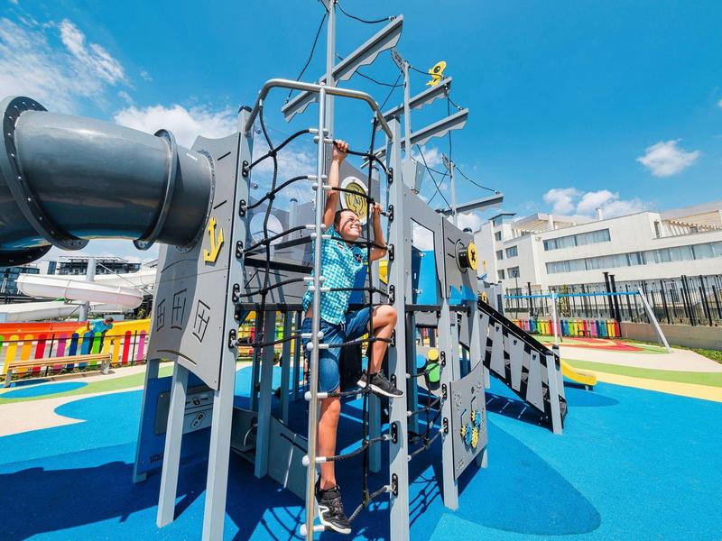 Enfant escaladant une structure de jeu avec toboggan dans l'aire de jeux extérieure colorée de l'hôtel.