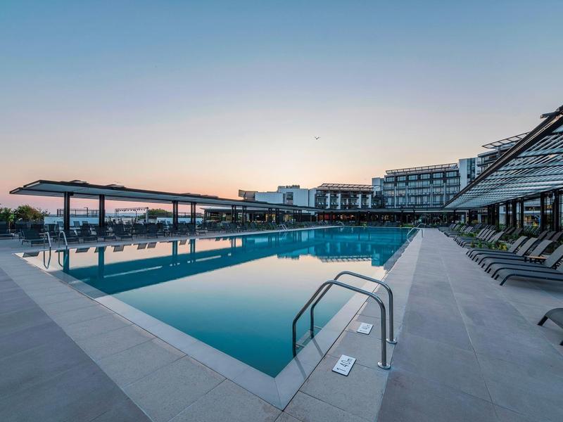 Piscine extérieure moderne avec chaises longues au coucher du soleil dans une station hôtelière.