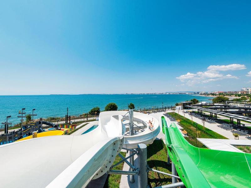 Les toboggans aquatiques donnent sur la mer et un paysage de plage lumineux et ensoleillé.