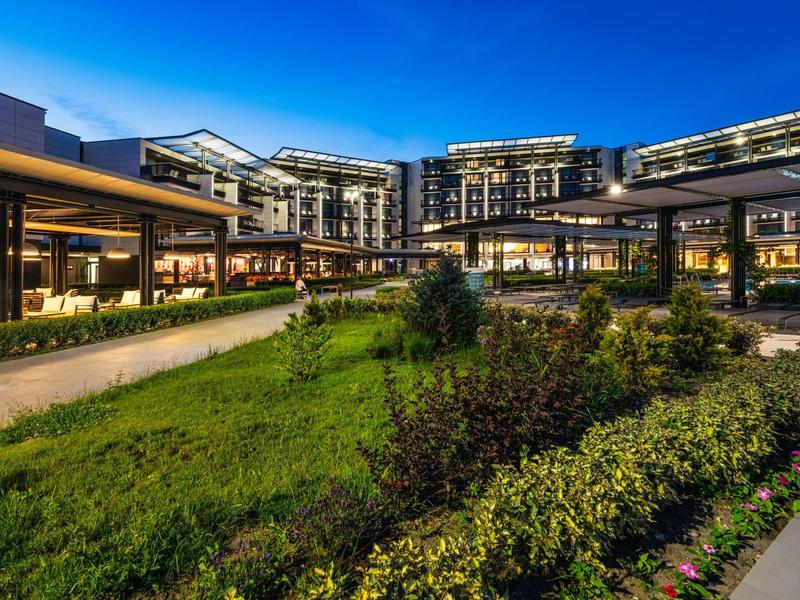 Complexe hôtelier moderne avec bâtiments éclairés et jardin bien entretenu au crépuscule.