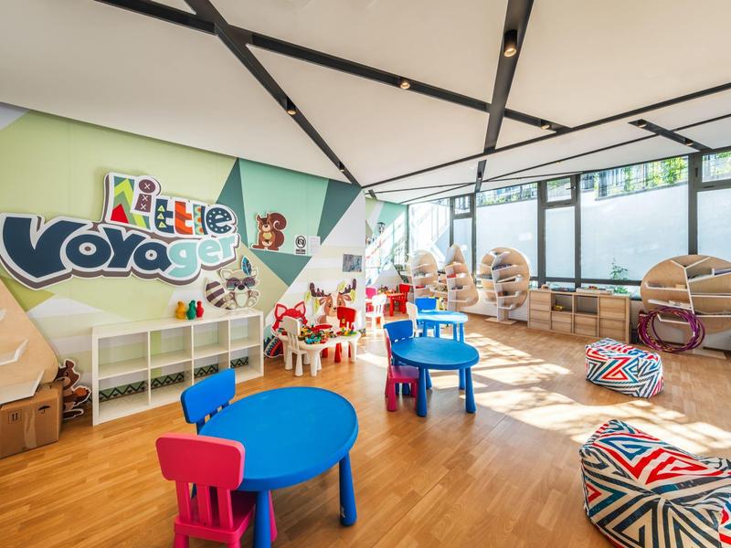 Salle de jeux lumineuse avec tables colorées, coussins et étagères pour enfants dans un hôtel.