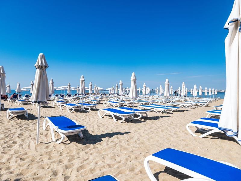 Chaises longues bleues vides et parasols blancs fermés sur une plage de sable sous un ciel bleu clair
