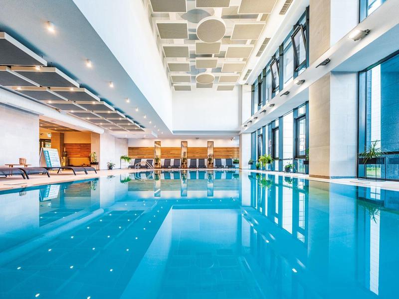 Piscine intérieure dans un hôtel moderne avec de grandes fenêtres et des chaises longues.