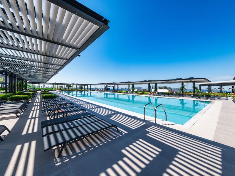 Piscine extérieure moderne avec espace lounge sous un pare-soleil à lames par ciel clair.