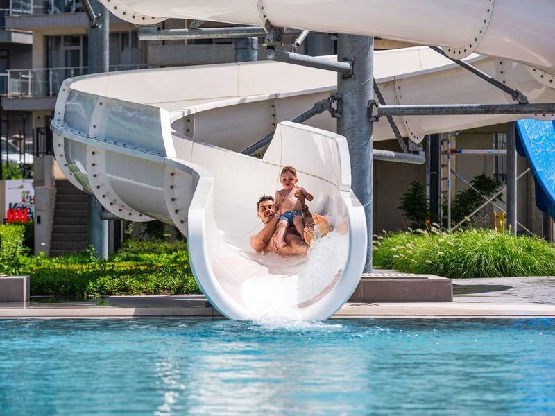 Deux personnes descendent ensemble un toboggan aquatique vers une piscine d'hôtel.