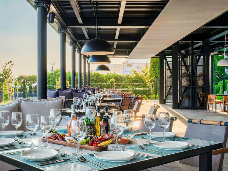 Terrasse élégamment dressée avec table à manger, verres et vue sur la verdure au coucher du soleil.
