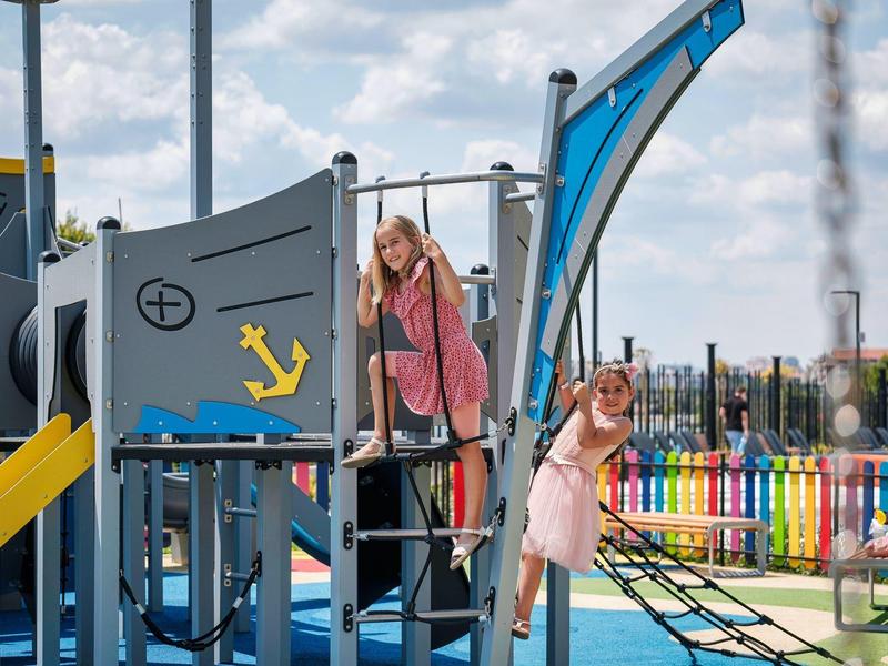 Enfants jouant sur une aire de jeux colorée avec structure et toboggan par temps ensoleillé.