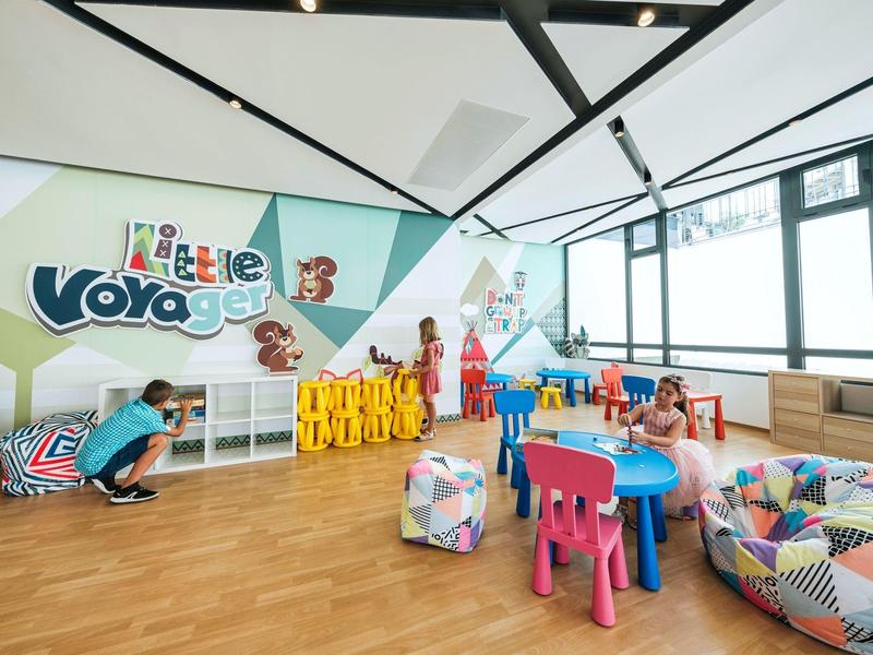 Salle de jeux colorée pour enfants avec tables, chaises et poufs dans un espace lumineux.