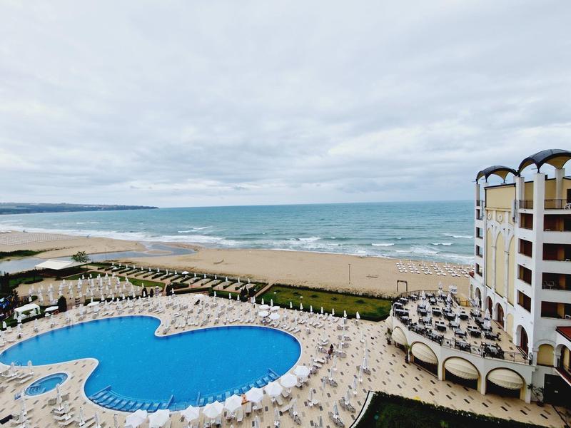 Hotel met groot zwembad, ligstoelen en uitzicht op het strand onder bewolkte lucht