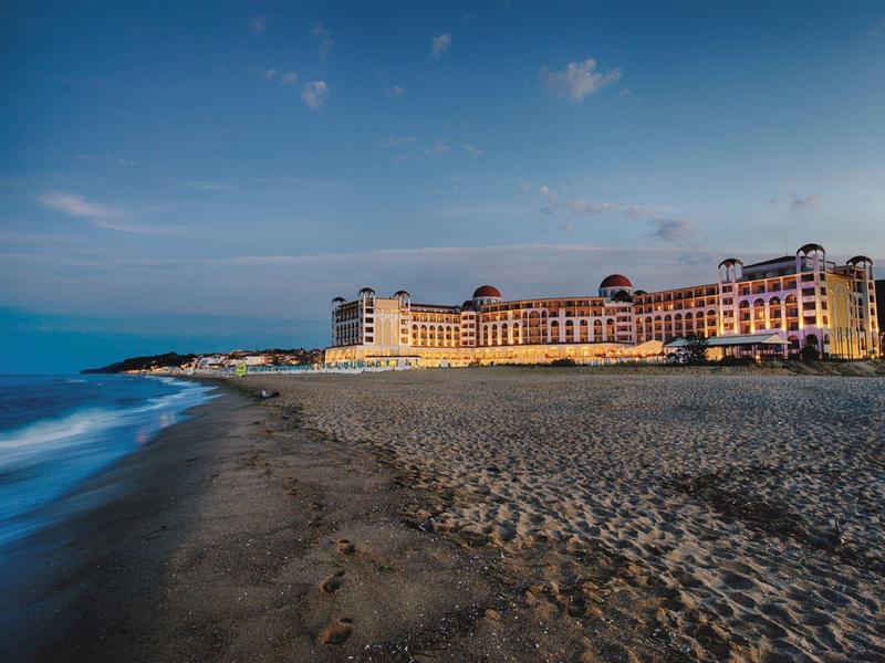Groot hotelgebouw op zandstrand bij schemering onder een blauwe lucht.