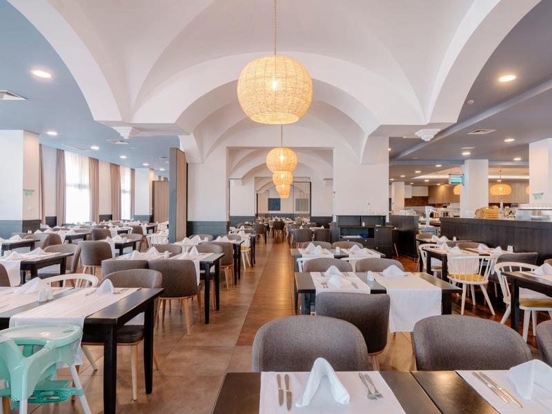 Ruim, licht hotelrestaurant met witte tafels en grijze stoelen onder gewelfde plafonds.