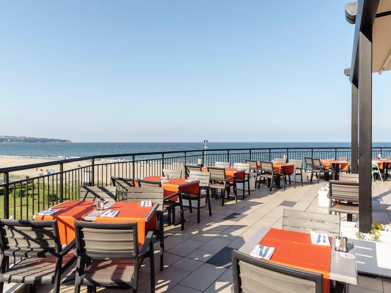 Terras met tafels en stoelen met uitzicht op zee en het zandstrand.