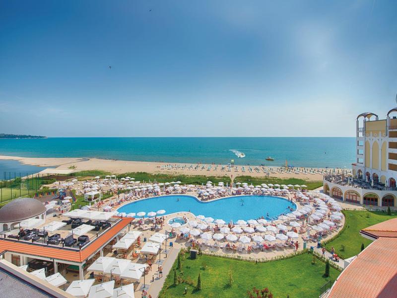 Hotel met groot zwembad, omgeven door ligstoelen en uitzicht op zee en strand.