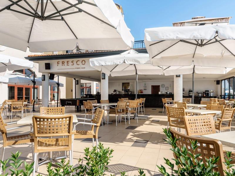 Leeg buitencafé met houten tafels en stoelen onder witte parasols.