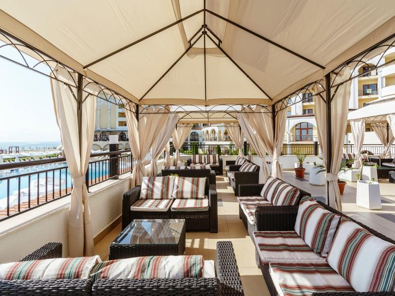 Gezellige zithoek onder een prieel met uitzicht op water en hotelbalkons.