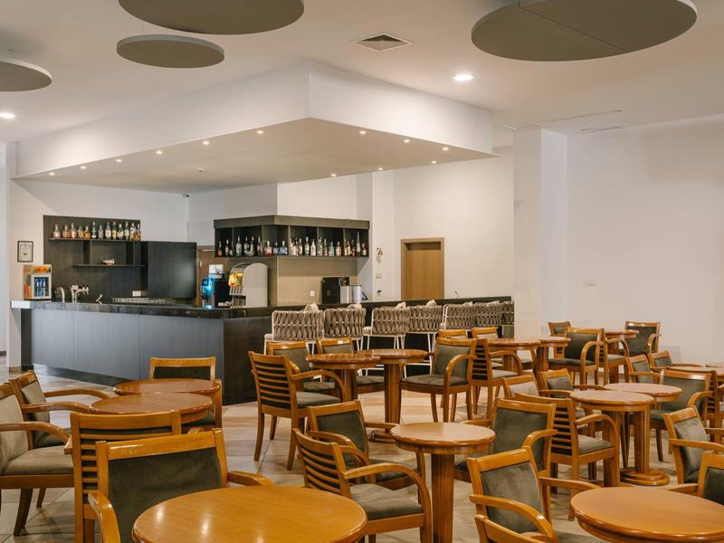 Moderne ontbijtruimte met houten tafels en stoelen, bar op de achtergrond.