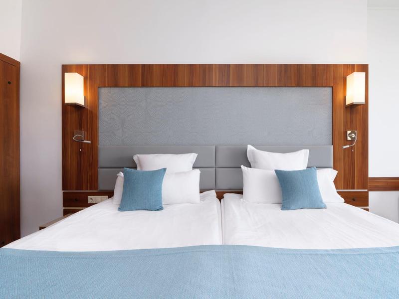 Moderne hotelkamer met twee eenpersoonsbedden, lichte muren en stijlvolle blauwe accenten.