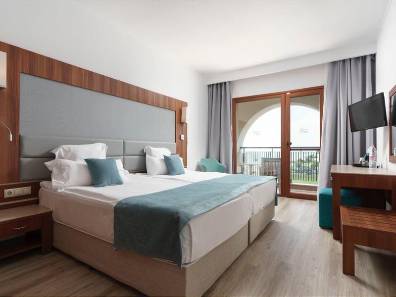 Lichte hotelkamer met twee eenpersoonsbedden, houten meubels en balkon met groen uitzicht.