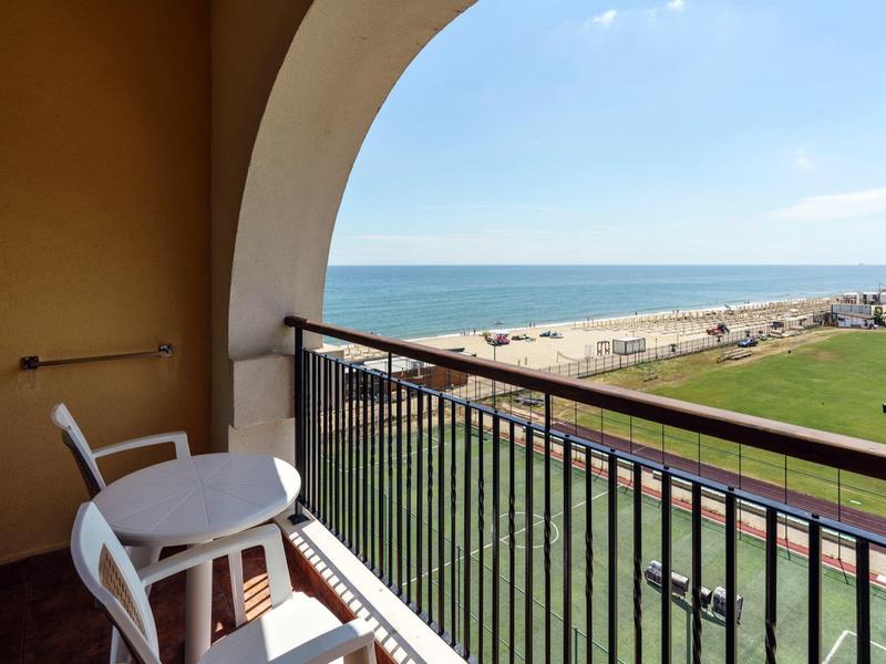 Balkon met witte stoelen en tafel met uitzicht op strand en zee bij heldere lucht.