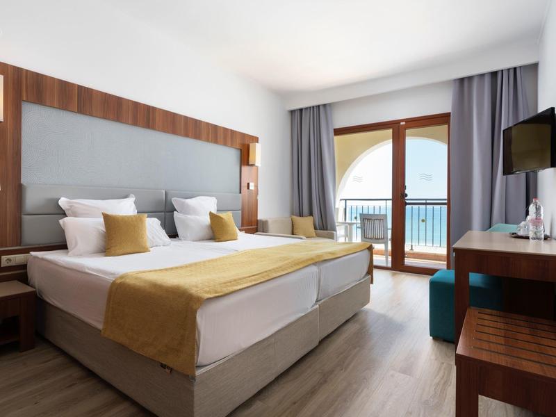 Moderne hotelkamer met tweepersoonsbed, balkon en zeezicht.