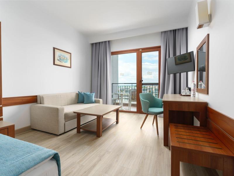 Lichte hotelkamer met bank, kleine tafel, tv en balkon met uitzicht.