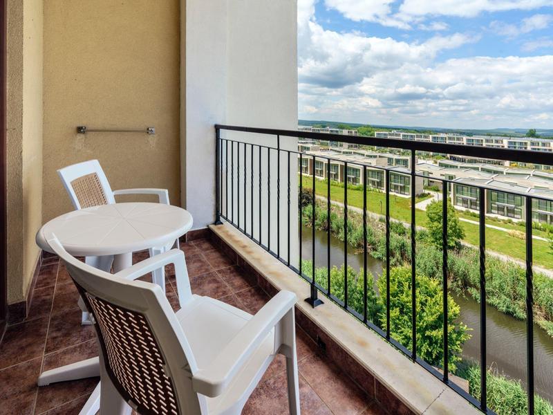 Balkon met twee stoelen en tafel met uitzicht op groen en water.