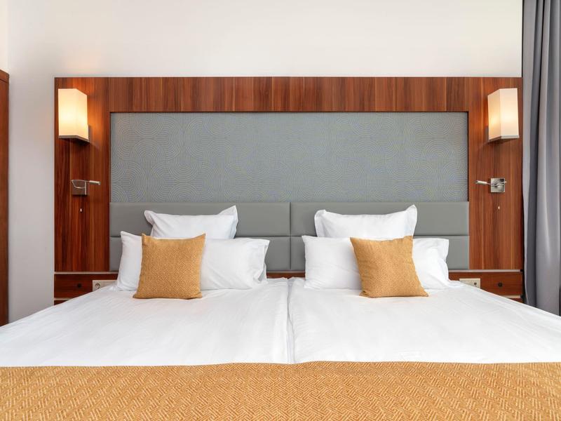 Twee-persoonskamer met wit beddengoed, oranje kussens en houten wandaccenten.