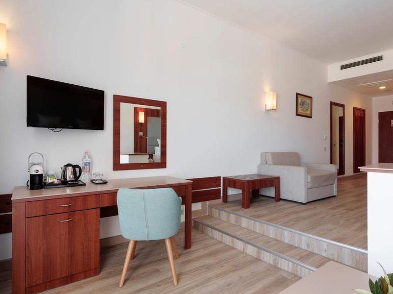 Modern ingerichte hotelkamer met bureau, tv en zithoek in neutrale kleuren.