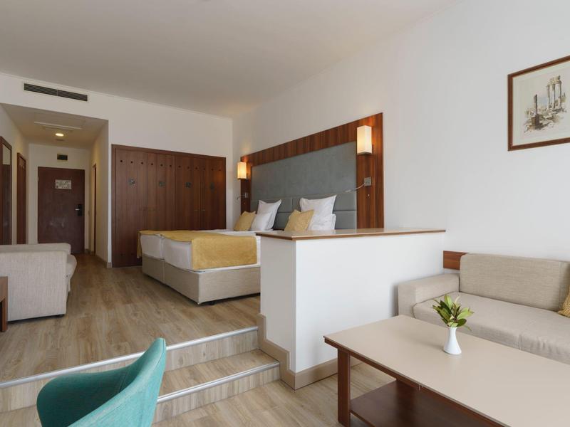 Lichte hotelkamer met tweepersoonsbed, zithoek en moderne inrichting.