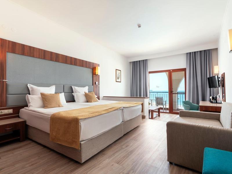 Gezellige hotelkamer met groot bed, zithoek en zeezicht door glazen deuren.