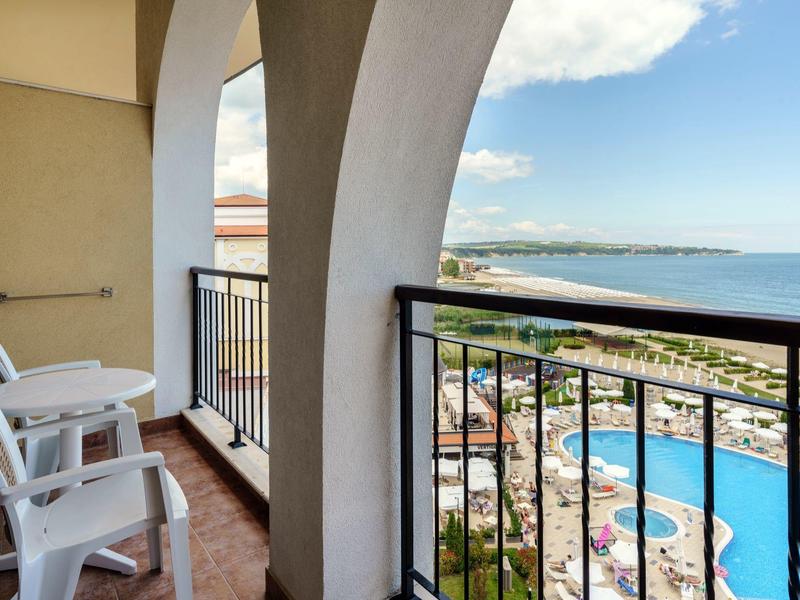 Balkon met witte stoelen en uitzicht op zwembad en zee bij helder weer.