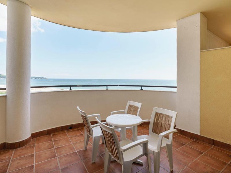 Balkon met terracotta vloer, witte tafel en vier stoelen met uitzicht op zee.