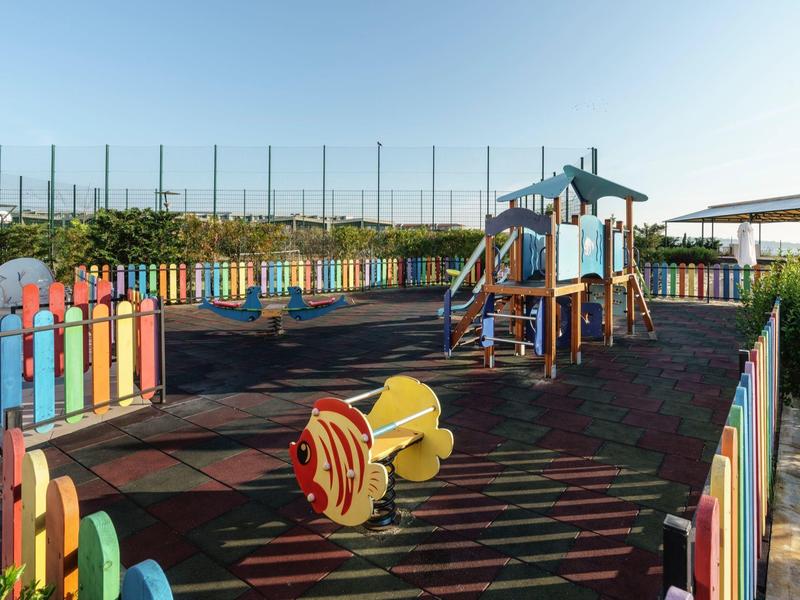 Een kleurrijke speeltuin met klimrek en houten hek onder een heldere lucht.