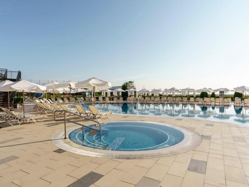 Groot zwembad met parasols en ligbedden onder heldere hemel.