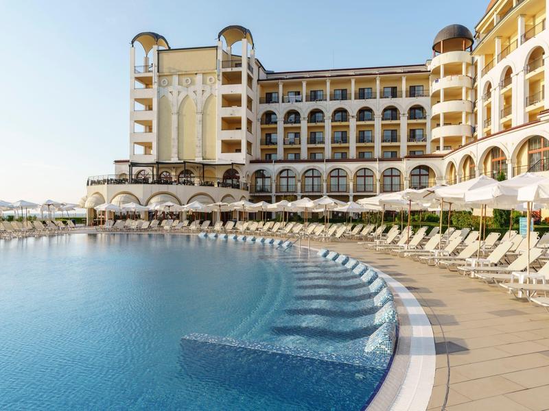 Luxe hotel met groot buitenzwembad en veel ligstoelen langs de rand van het zwembad bij zonnig weer.