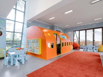 Lichte speelruimte voor kinderen met oranje speelhuis en knutseltafel in lichte kamer met grote ramen.