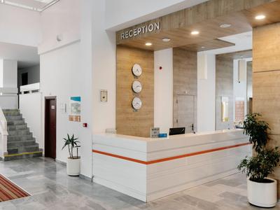 Helle Hotelrezeption mit weißer Theke, hölzernen Akzenten und Pflanzen.